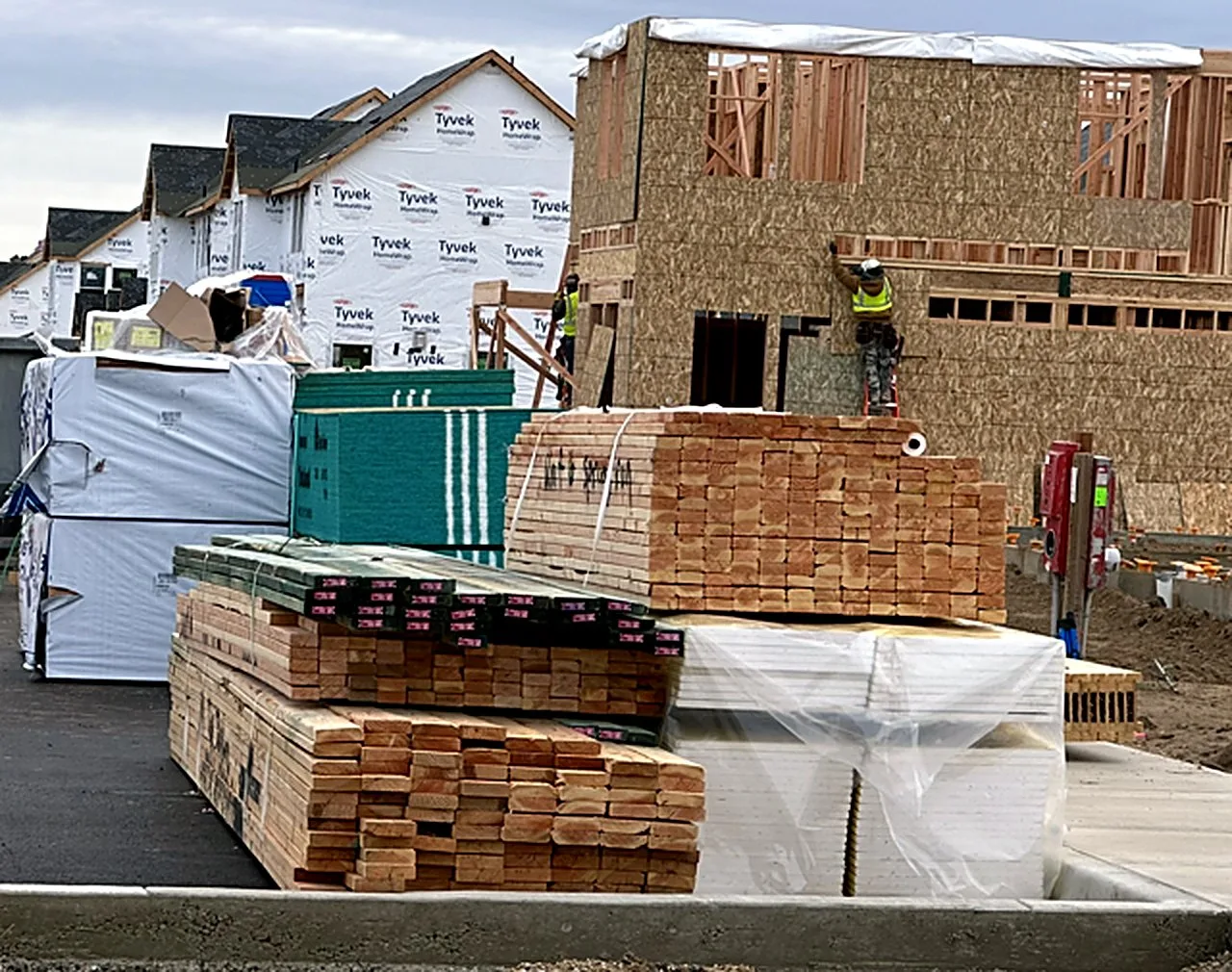 Lumber package stacked on site while a framer works on the wall behind
